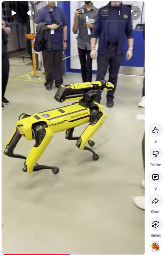 A video still from a Youtube Short. On screen is a yellow Boston Dynamics robot walking among a group of students. 