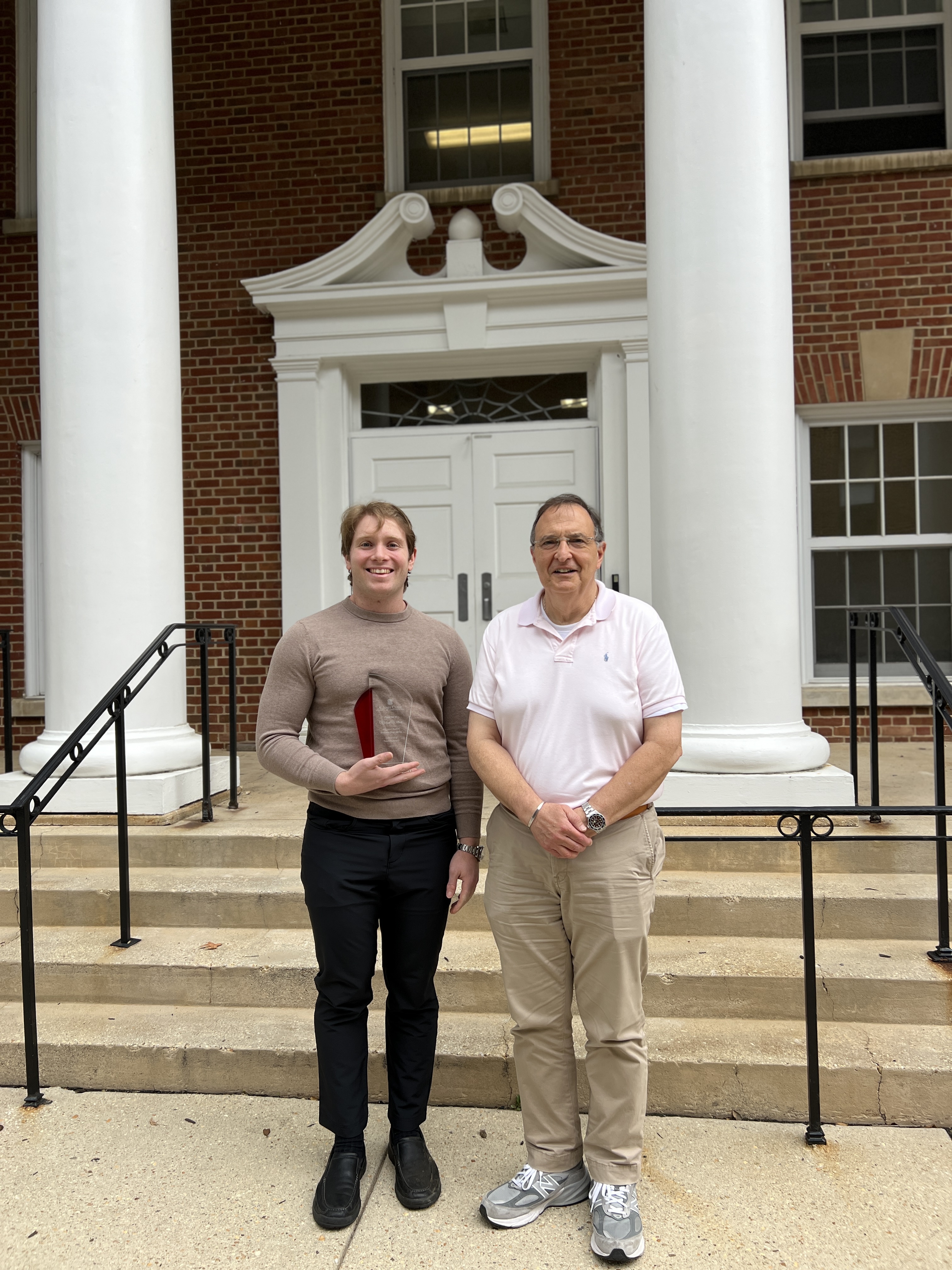 Two MAGE faculty standing outside of J.M. Patterson Building, one is holding an award.